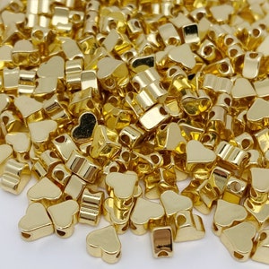 May include: A large pile of gold heart-shaped metal beads. The beads have a shiny finish and are ideal for jewellery making or crafting.