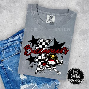 May include: A gray t-shirt with a graphic design of a skull and crossbones with a pirate hat, a checkered lightning bolt, and the text "Buccaneers" in red and white. The design is surrounded by five black stars.