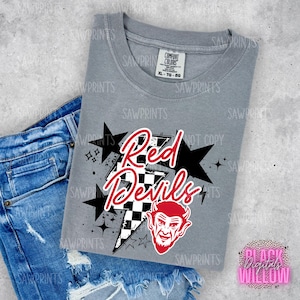 Op de afbeelding: Grijs T-shirt met een rood en zwart grafisch ontwerp met de tekst "Red Devils" met een geruit patroon en een rood duivelshoofd. De grafiek is omringd door sterren.