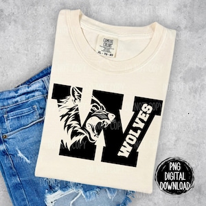 Könnte beinhalten: Ein weißes T-Shirt mit einer schwarzen Grafik eines Wolfskopfes in einem großen schwarzen Buchstaben W. Der Text "WOLVES" ist vertikal auf der rechten Seite des Buchstabens W geschrieben.