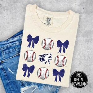 May include: A cream-colored t-shirt with a blue wolf graphic, baseballs, and blue bows. The text "COMFORT COLORS" and "XL - TO - EG" is printed on the shirt.