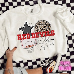 May include: White sweatshirt with a black star, a basketball with a leopard print, and the text "RED DEVILS" in red. The design also includes a basketball hoop and stars.