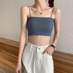 May include: A light blue ribbed crop top with thin spaghetti straps. The top is worn with white high-waisted jeans.