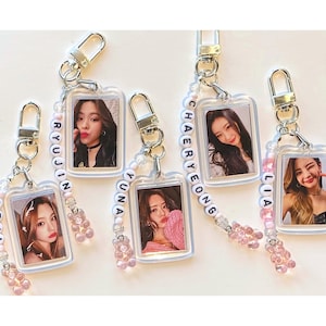 May include: Five clear plastic keychains with small photo cards of five different women. Each keychain has a beaded charm with the name of the woman in the photo spelled out in white letters.