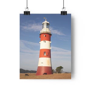 Puede incluir: Impresión en póster de un faro a rayas rojas y blancas, bajo un cielo azul con nubes dispersas. El faro tiene una linterna blanca y una pequeña veleta dorada. Dos bancos están en primer plano sobre una colina cubierta de hierba.