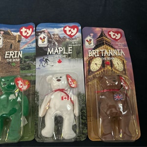 May include: Three Ty Beanie Baby plush toys in their original packaging. The toys are Erin the Bear, Maple the Bear, and Britannia the Bear. Erin is green with a shamrock, Maple is white with a Canadian flag, and Britannia is brown with a Union Jack flag.