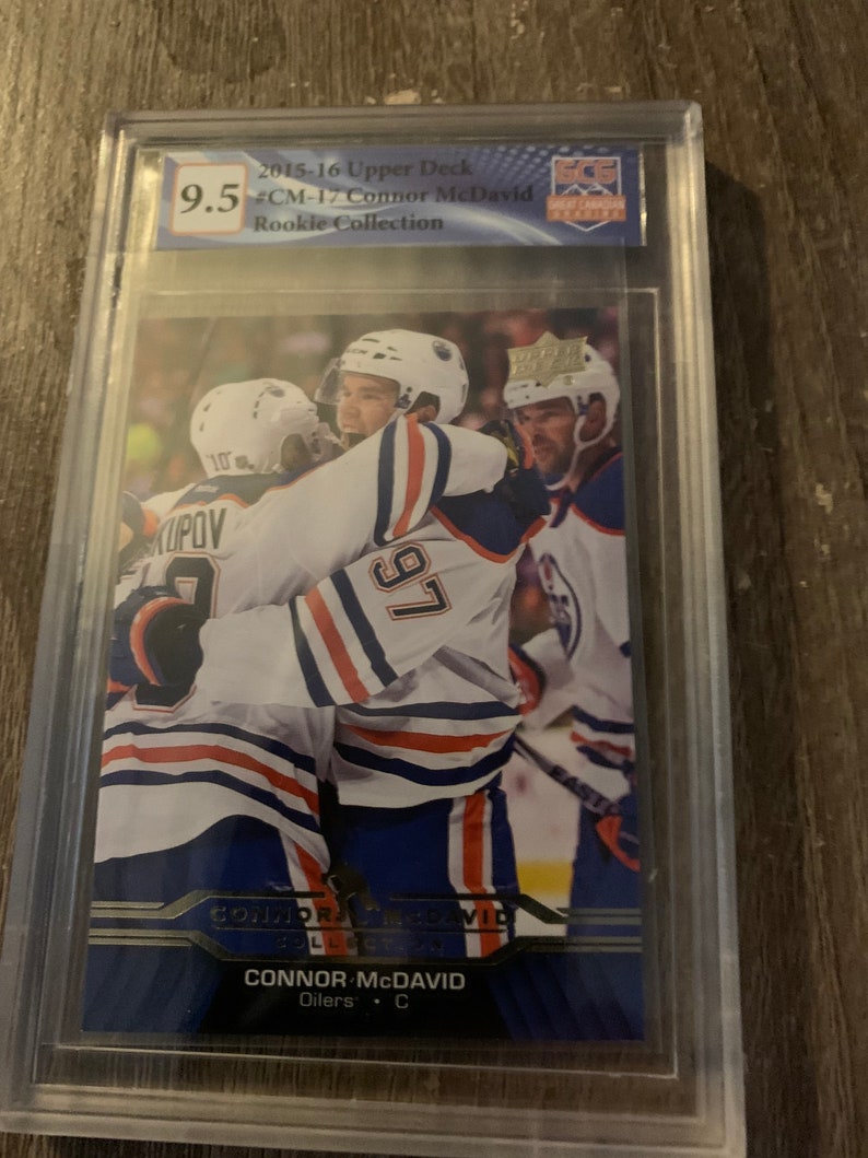 Puede incluir: Una tarjeta de hockey clasificada con Connor McDavid, un jugador de los Edmonton Oilers. La tarjeta es del set Rookie Collection Upper Deck 2015-16 y est&aacute; clasificada con un 9,5 por Beckett Grading Services.