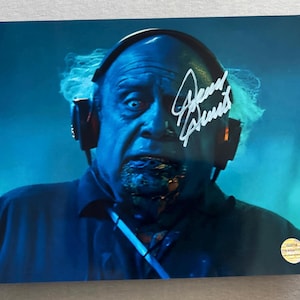May include: A close-up of a man with a blue and white face, wearing headphones and a dark blue shirt. The man is looking at the camera and has a signature that says "Brent Spiner" on the image.