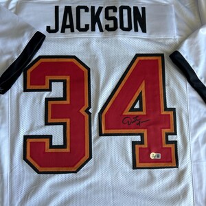 May include: White mesh jersey with the name "JACKSON" across the back and the number "34" in red with black and gold trim. The jersey has red and gold accents on the shoulders and a black collar.