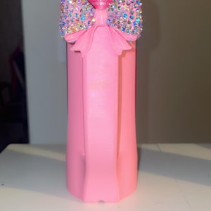 Pu&ograve; includere: Un portabevande rosa con un ornamento a fiocco scintillante. Il fiocco &egrave; adornato con strass iridescenti. Il portabevande &egrave; progettato per mantenere fresche le bevande.