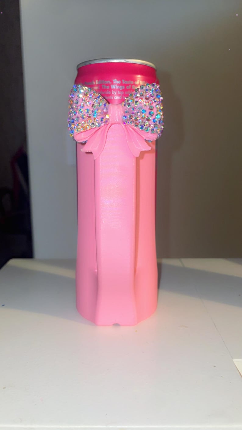 Pu&ograve; includere: Un portabevande rosa con un ornamento a fiocco scintillante. Il fiocco &egrave; adornato con strass iridescenti. Il portabevande &egrave; progettato per mantenere fresche le bevande.