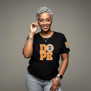 May include: Black t-shirt with the word "DOPE" in orange block letters. The shirt also features a circular logo and a small emblem on the sleeve. The person in the image is wearing glasses and jewelry.