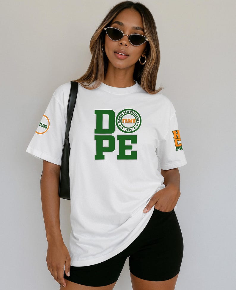 May include: White t-shirt with the word "DOPE" in large green block letters. Above the "PE" is a circular emblem with text. The shirt also has text on the sleeves. The person is wearing black shorts and sunglasses.