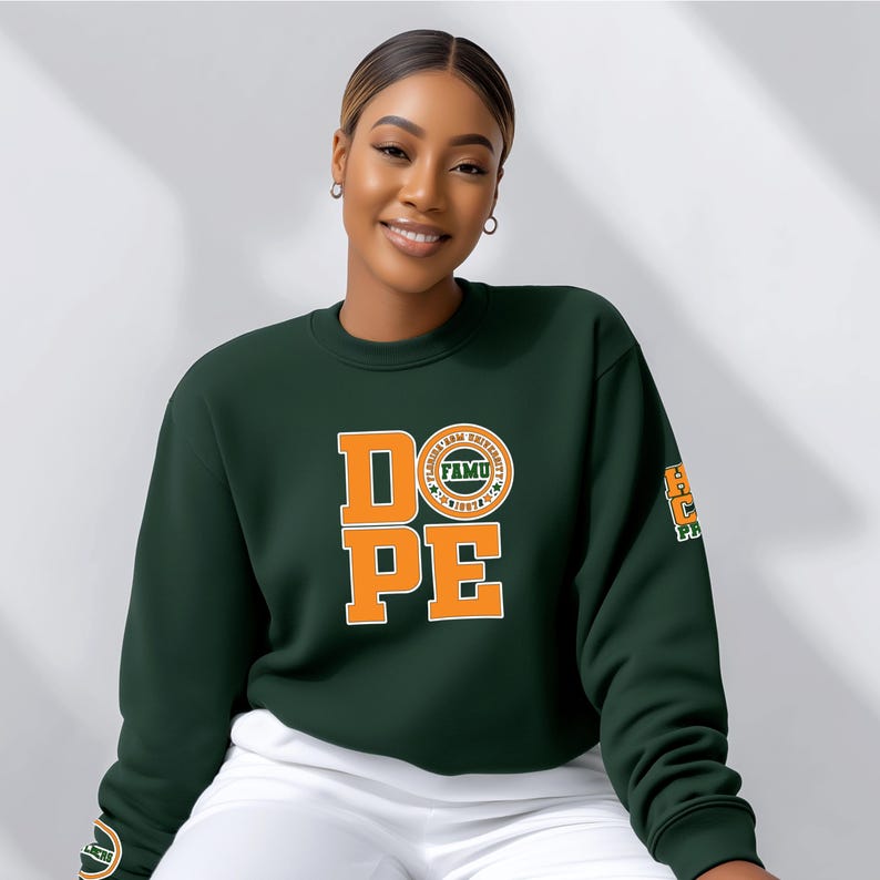 May include: A dark green sweatshirt with the word "DOPE" in orange block letters. The letter "O" features a circular emblem with the text "FAMU" and "Florida A&M University". The right sleeve has an orange and green emblem. The sweatshirt is paired with white pants.