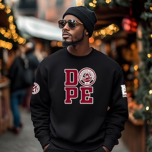May include: Black sweatshirt with the word "DOPE" in maroon block letters and a white outline. The sweatshirt also features the words "Morehouse College 1867" in a circular emblem. A black beanie and sunglasses are also visible.