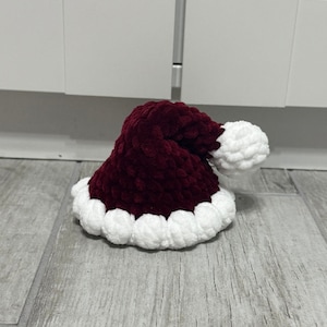 May include: A plush, burgundy Santa hat with a white, fluffy trim and a matching pom-pom. The hat is made of a soft, textured material, perfect for holiday celebrations and festive occasions.