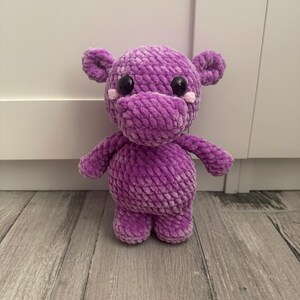 May include: A purple crocheted hippopotamus stuffed animal with black eyes and pink cheeks.