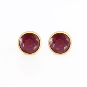 May include: A pair of gold stud earrings with red gemstone accents.