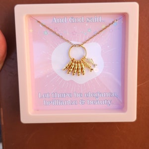 May include: A gold necklace with a charm that says "And God said... Let there be elegance, brilliance & beauty."