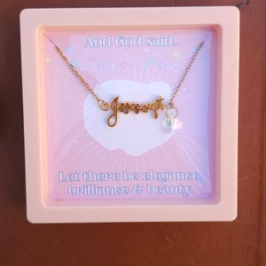 May include: A pink box with a gold necklace that says "Jesus wept" with a clear crystal charm. The box has the text "And God said... Let there be elegance, brilliance & beauty."