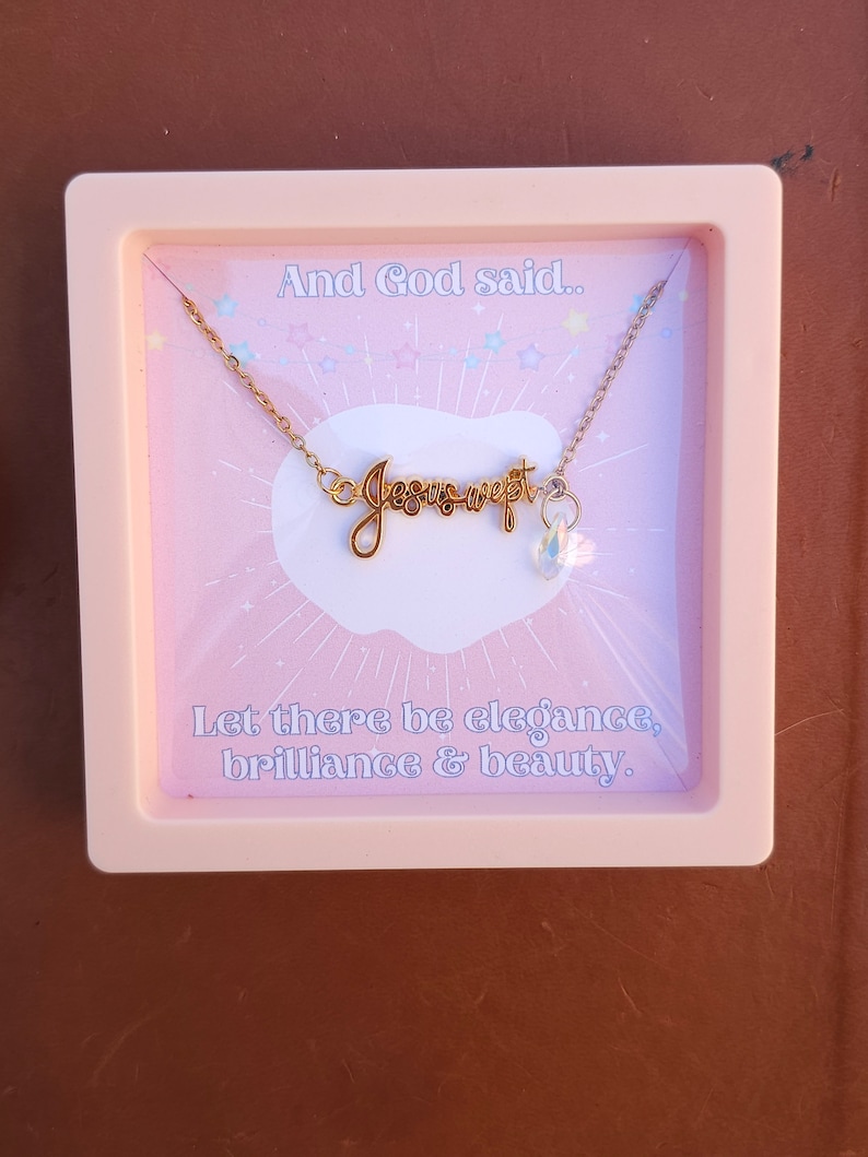 May include: A pink box with a gold necklace that says "Jesus wept" with a clear crystal charm. The box has the text "And God said... Let there be elegance, brilliance & beauty."