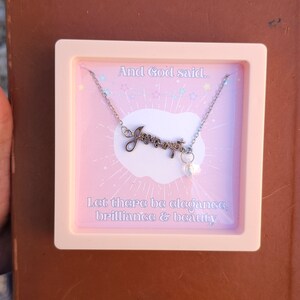 May include: A pink box with a silver necklace inside. The necklace has a charm that says "Jesus wept" and a small pearl charm. The box has the text "And God said... Let there be elegance, brilliance & beauty."