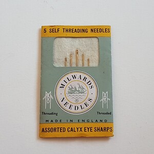 Könnte beinhalten: Eine Packung mit 5 selbst-fädelnden Nadeln, hergestellt in England von Milwards. Die Verpackung ist grün und gelb mit einem weißen Etikett, auf dem "Milwards Needles" und ein Bild eines Schiffes steht. Das Etikett trägt außerdem die Aufschrift "Assorted Calyx Eye Sharps".