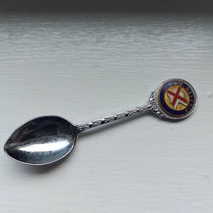 May include: A silver souvenir spoon with a blue and white enamel circle featuring a red cross and the text "MY DEVON" on the handle.