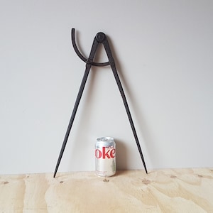 May include: A large, antique, black metal compass with a long, pointed leg on each side. The compass is about the size of a soda can.