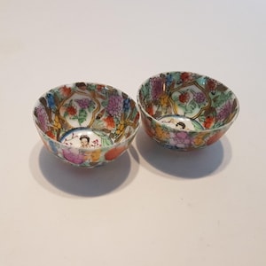 May include: Two small, round decorative bowls with a colourful floral design. The bowls feature a variety of colours, including red, purple, yellow, and green. Each bowl has a small figure in the centre.