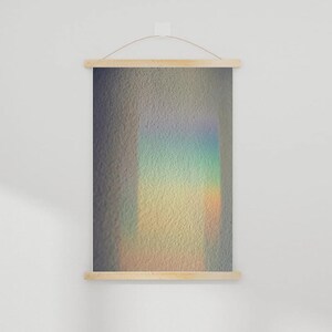 Puede incluir: Un tapiz rectangular con marco de madera y un patrón de luz de colores del arcoíris. El patrón de luz es un rectángulo vertical con colores que van del azul al amarillo. El tapiz está suspendido por una varilla de madera y una cuerda.