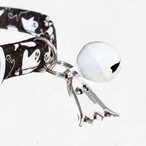 A black and white ghost-themed collar tag with a bell attached to it.