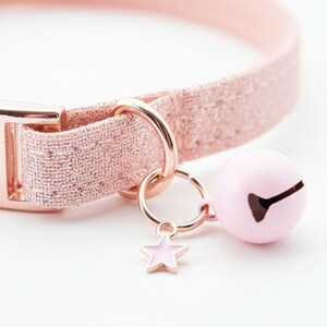 A pink glittery collar with a bell charm and a star charm attached to it.
