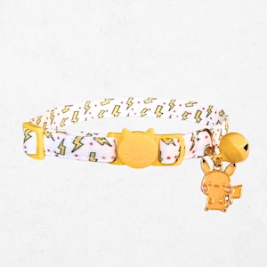 A white cat collar with yellow lightning bolt patterns and a bell charm featuring a Pikachu character.