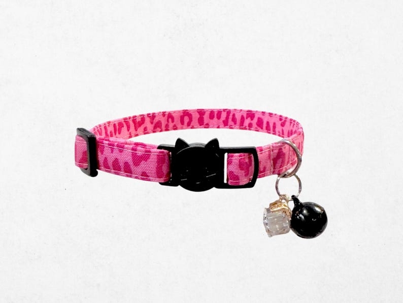 A pink leopard print cat collar with a black buckle and bell attached.