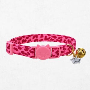 A pink cat collar with a bell and a charm featuring a cat's face.