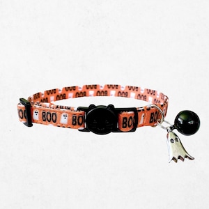 A cat collar with a bell and a charm featuring the word "BOO" printed on it.