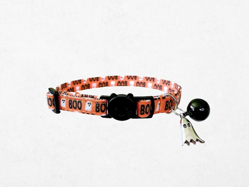 A cat collar with a bell and a charm featuring the word "BOO" printed on it.