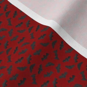 a close-up view of a fabric with a repeating pattern of bats in black and red colors. The fabric appears to be a red background with a white border, creating a striking contrast between the two colors.