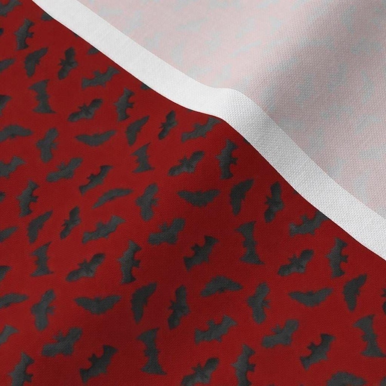 a close-up view of a fabric with a repeating pattern of bats in black and red colors. The fabric appears to be a red background with a white border, creating a striking contrast between the two colors.