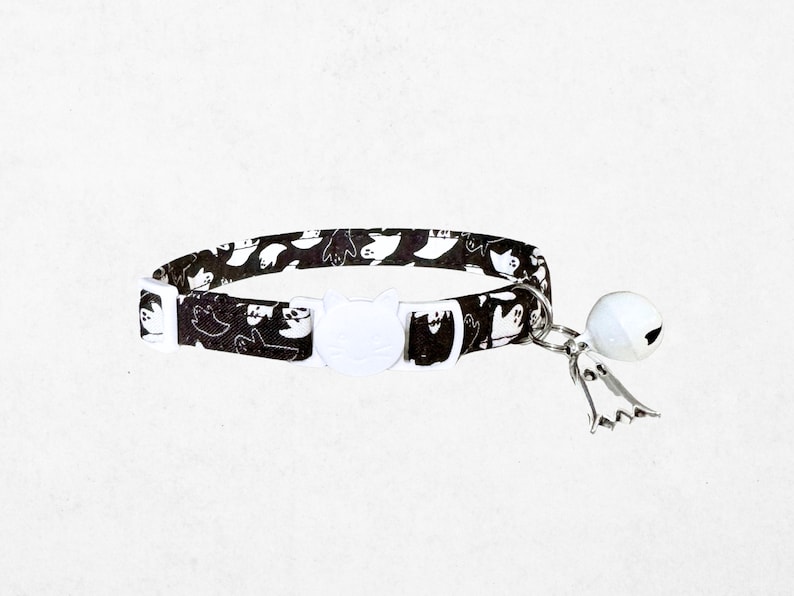A black and white cat collar with a bell attached, featuring a repeating pattern of cat silhouettes.