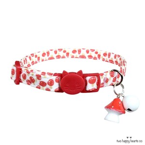 Puede incluir: Collar para gatos rojo y blanco con estampado de fresas. El collar tiene una hebilla roja con forma de gato y un charm de seta con una campana. El collar mide aproximadamente 30 cm de largo.