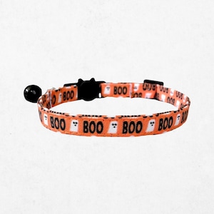 A cat collar with a repeating pattern of the word "BOO" in black letters, along with ghost-like silhouettes in orange and white.