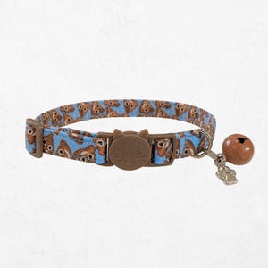 May include: A light blue pet collar featuring a repeating pattern of brown poop emojis. The collar includes a brown plastic buckle shaped like a cat face, a metal D-ring, a silver-toned paw print charm, and a small round brown bell attached to the side.