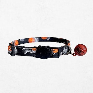 A black and orange cat collar with a basketball pattern and a red bell attached to it.