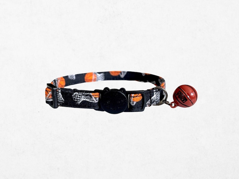 A black and orange cat collar with a basketball pattern and a red bell attached to it.
