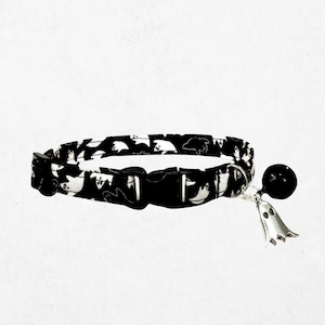 A black and white cat collar with a bell and a ghost charm.