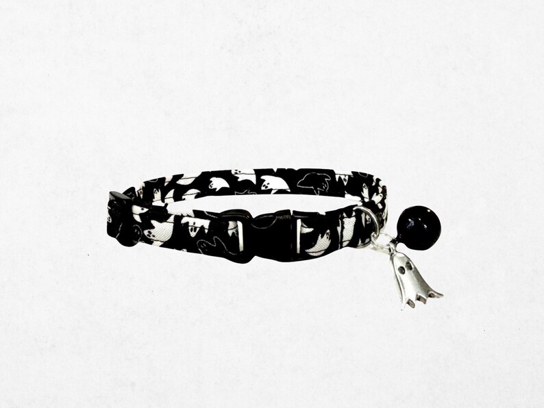 A black and white cat collar with a bell and a ghost charm.
