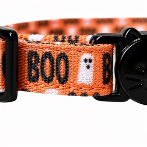 A close-up of a cat collar with a Halloween-themed design, featuring the word "BOO" and a ghost character.