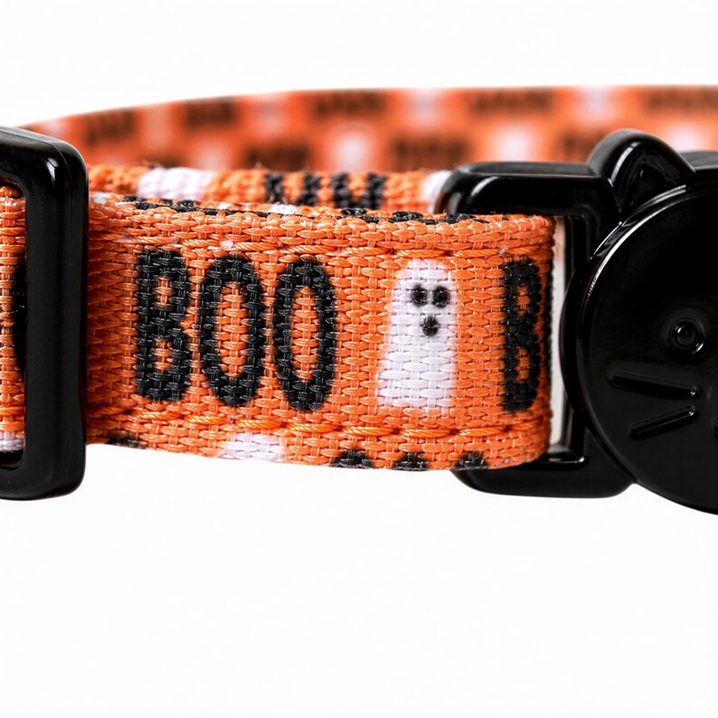 A close-up of a cat collar with a Halloween-themed design, featuring the word "BOO" and a ghost character.
